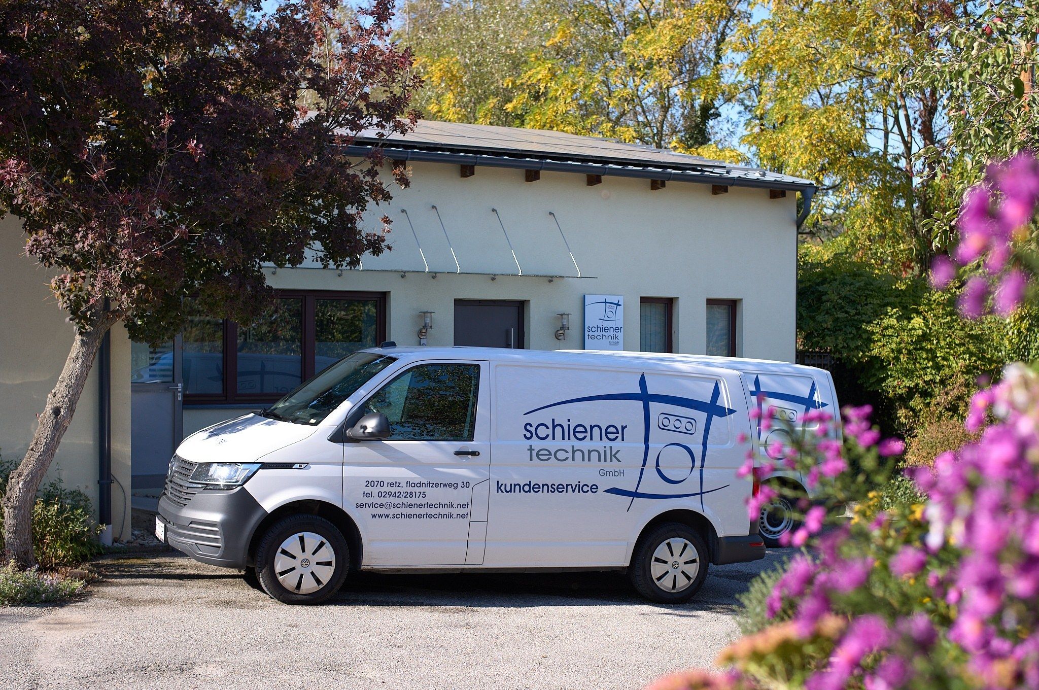 Servicefahrzeuge der schiener technik GmbH vor dem Firmengebäude in Retz, rechts blühende Herbstblumen